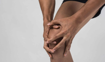 Young sport man with strong athletic legs holding knee with his hands in pain after suffering ligament injury  isolated on white.