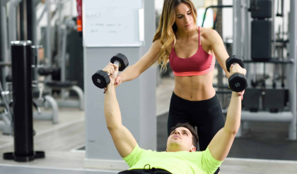 Female personal trainer helping a young man lift weights while working out in a gym