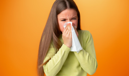 Teen,Girl,Blowing,Her,Nose,Against,Orange,Background